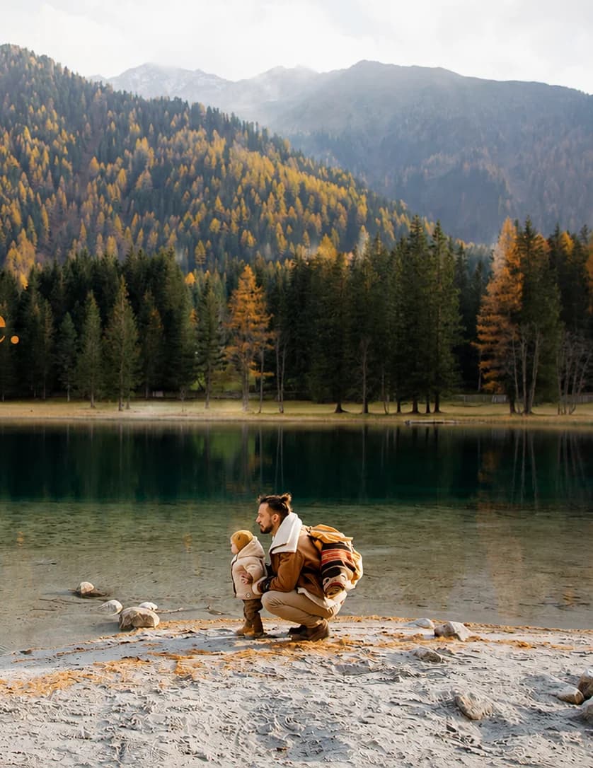 A father crouched beside his small child at the edge of a mountain lake.