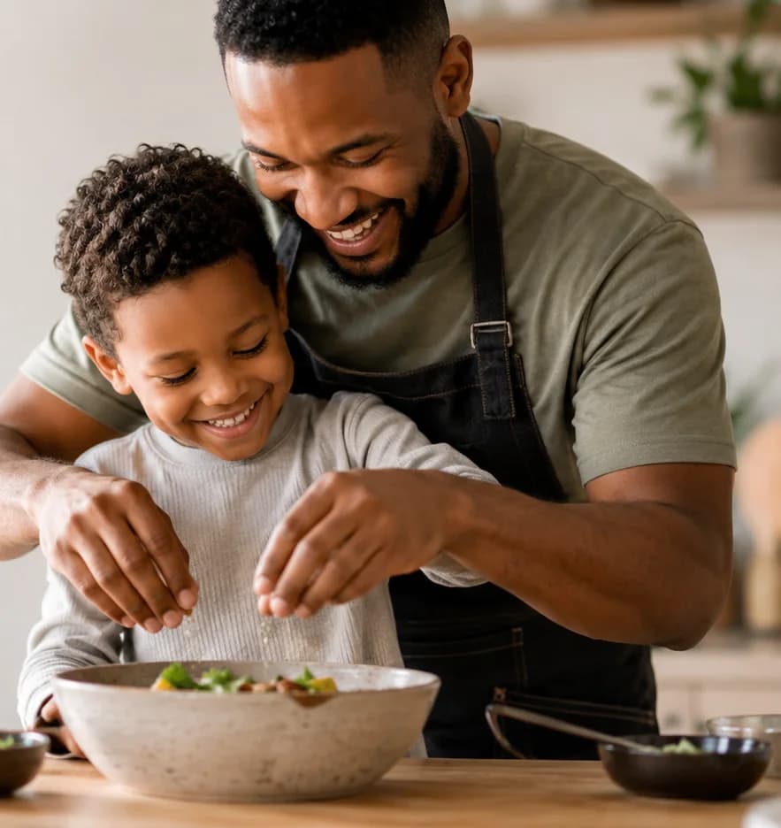 A father and his young son laughing together while they cook at the kitchen counter.
